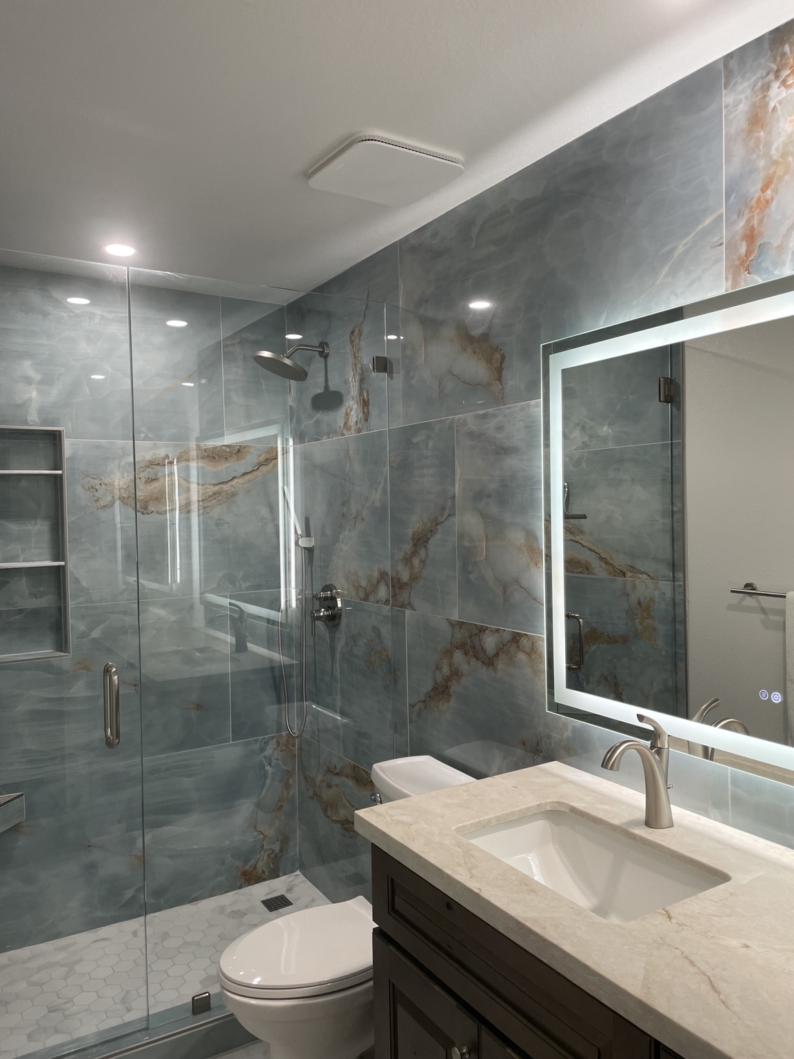 Completed bathroom with blue stone-look shower, glass enclosure, and illuminated mirror