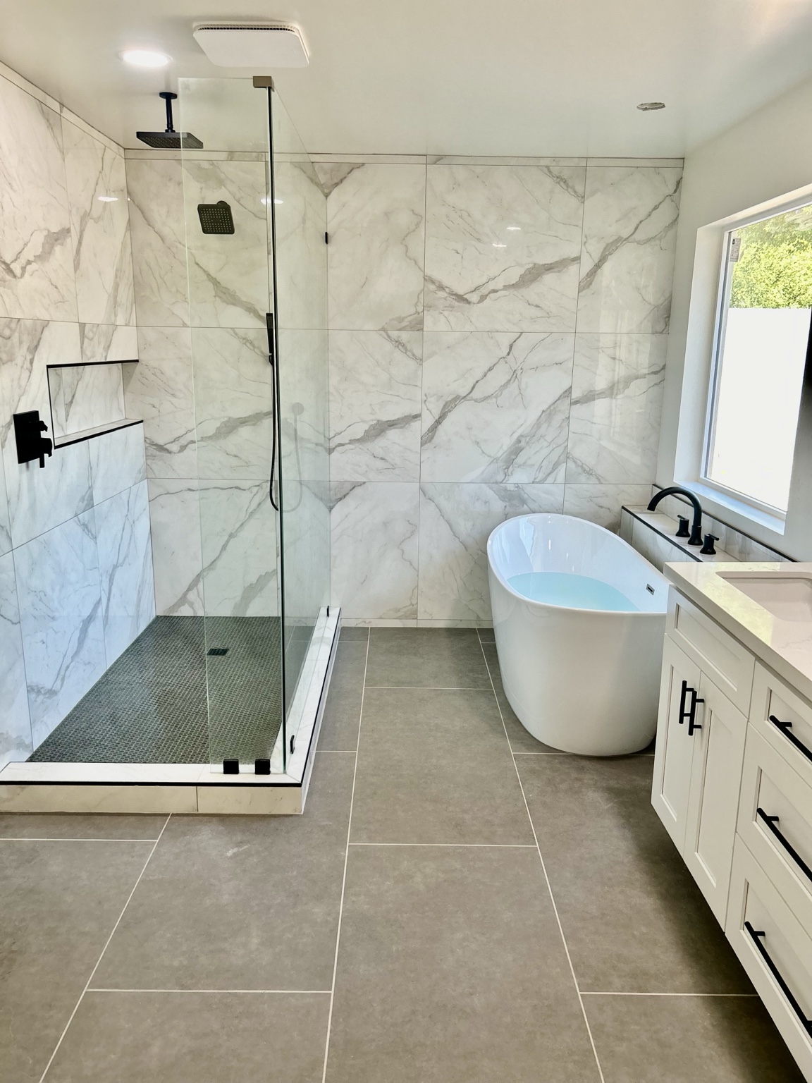 Completed bathroom with marble-look shower, freestanding tub, and black fixtures
